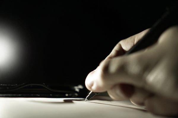 Person writing with a pen on a sheet of paper in a quiet environment.